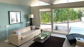 Een moderne woonkamer met een bank, salontafel en uitzicht op een tuin door grote ramen.