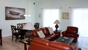 A living room with a brown leather sofa, a dining table with chairs, a coffee table, and a ceiling fan. - PRIVATE LUXURY, Beachfront Home, Hot Tub, Kayaks, Paddle Board, Cabana (Casuarina Point)