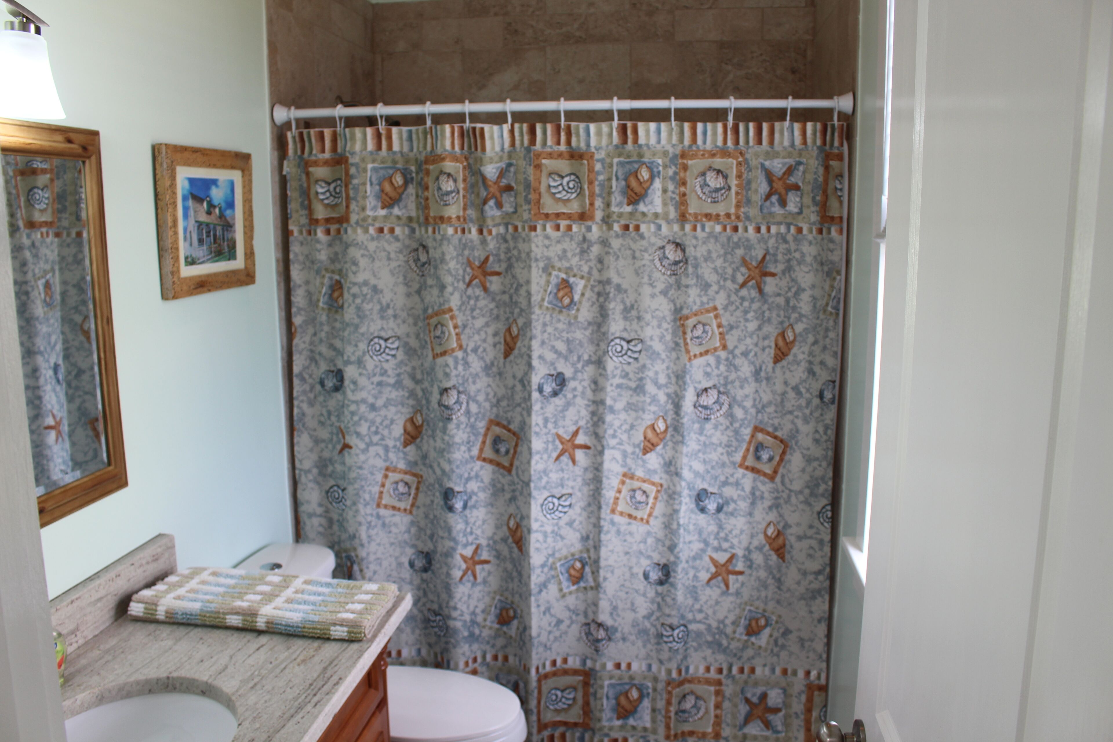 A bathroom with a shower curtain featuring a nautical pattern, a toilet, and a sink with a towel.
