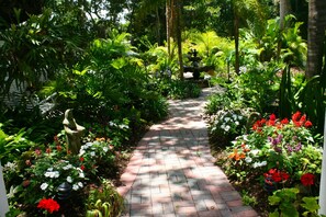 A garden pathway with a brick surface, surrounded by various plants and flowers. - "Your Own Private Resort" at 9 Oaks!            (New Smyrna Beach)