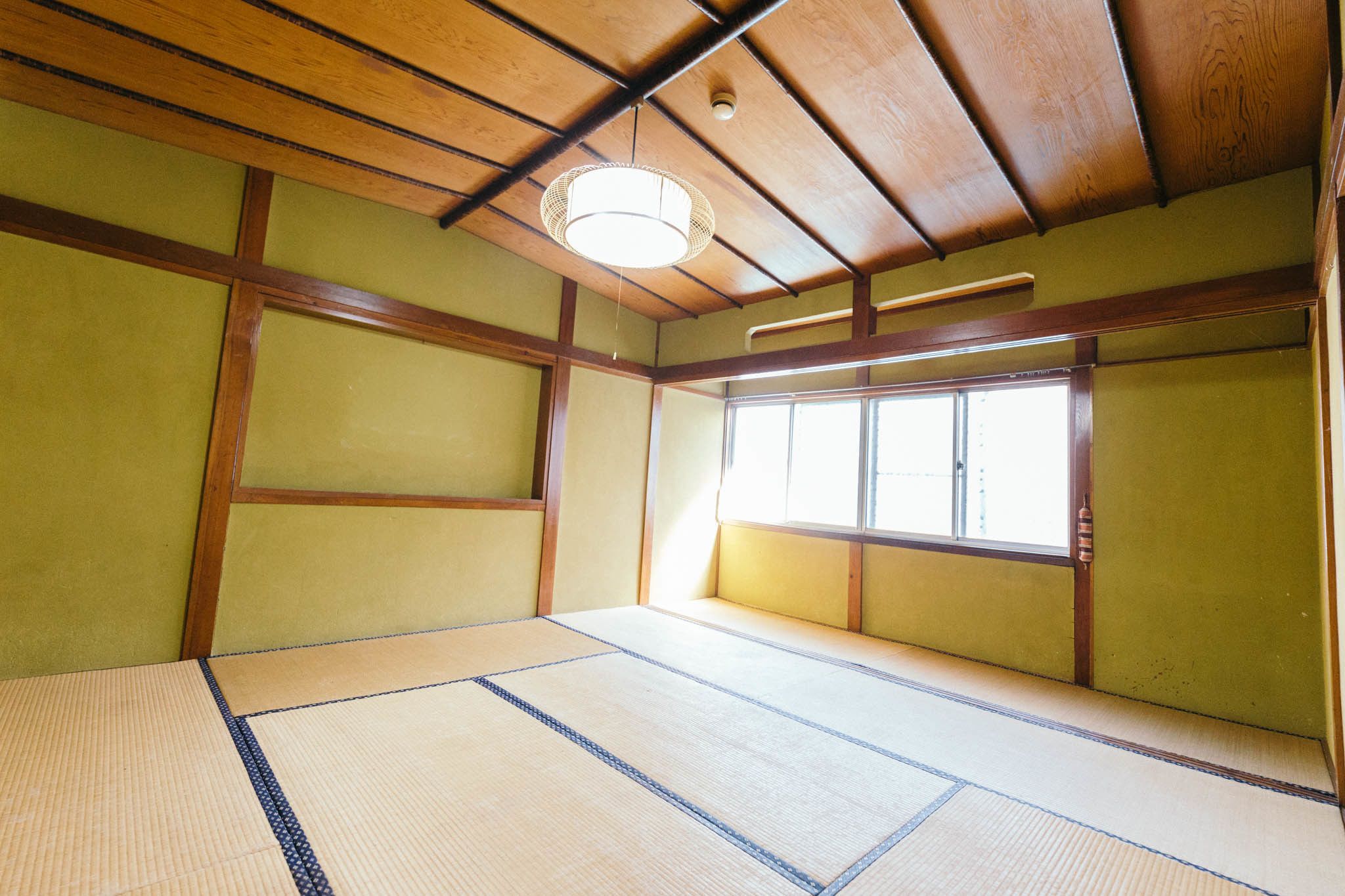 A tatami mat room with wooden beams, a ceiling light, and a window.