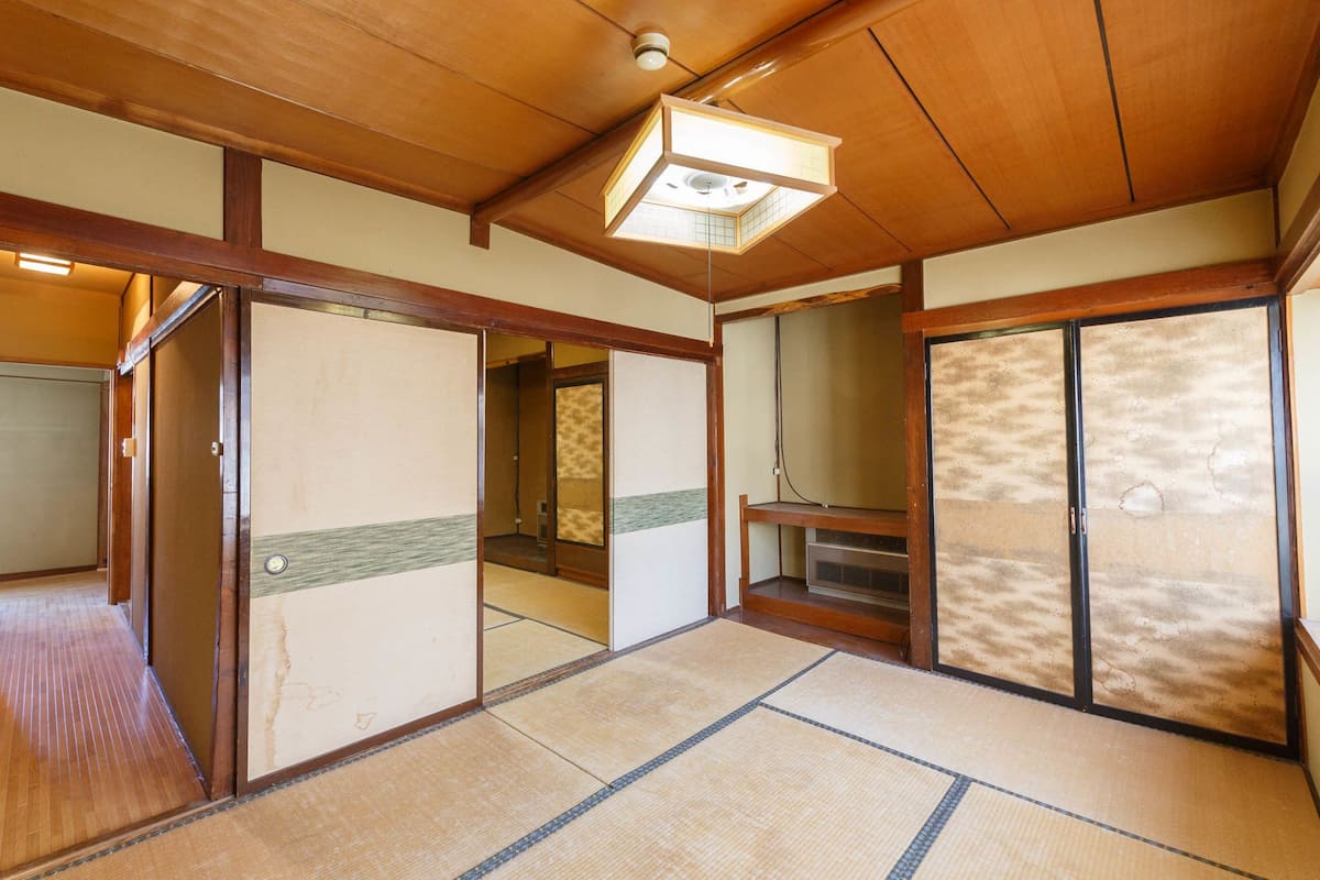 A traditional Japanese room with tatami flooring, sliding doors, and a ceiling light fixture.