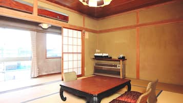 Una habitación tradicional japonesa con suelo de tatami, una mesa baja, un banco acolchado, una puerta corredera y un ventilador de techo.