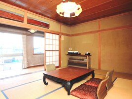 Una habitación tradicional japonesa con suelo de tatami, una mesa baja, un banco acolchado, una puerta corredera y un ventilador de techo.