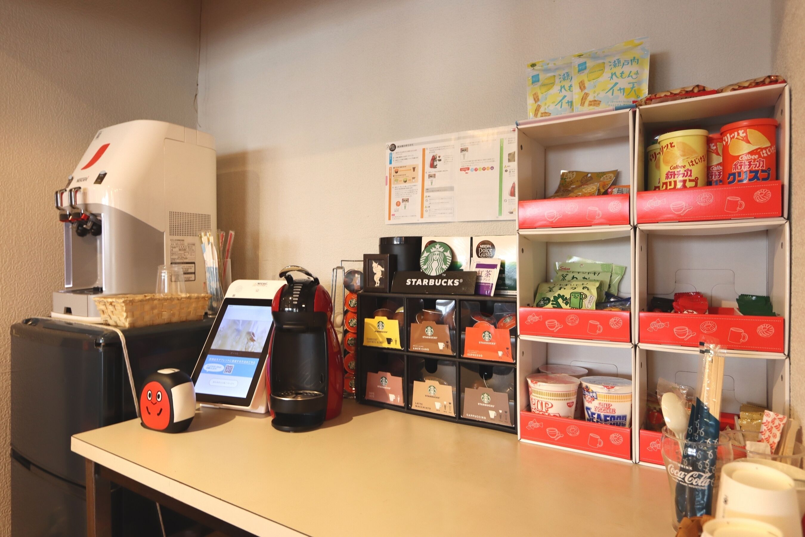 A coffee station with a coffee machine, a tablet, and a coffee cup. There are Starbucks branded items and a Coca-Cola bottle on the counter.