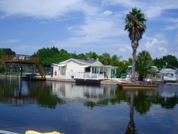 Een pand aan het water met een aanlegsteiger, een klein huis met veranda en een palmboom.