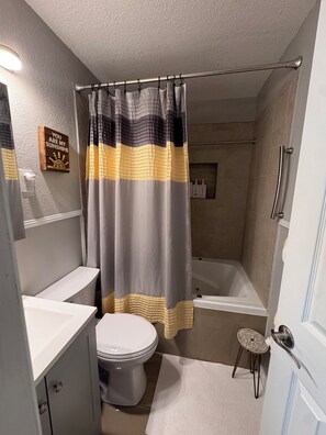 Een badkamer met douchegordijn, toilet, badkuip en een klein krukje.