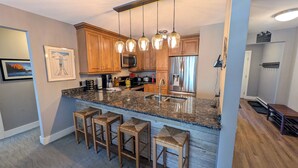 A kitchen with wooden cabinets, granite countertops, a stainless steel refrigerator, and pendant lighting. - Luxury Condo w/ FREE WiFi, Parking, Heated Pool, Hot Tubs, Skier Shuttles (Avon)