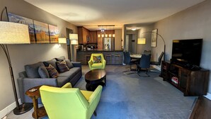 A living room with a sofa, armchairs, a coffee table, and a TV. There is a kitchen in the background with a dining area. - Luxury Condo w/ FREE WiFi, Parking, Heated Pool, Hot Tubs, Skier Shuttles (Avon)