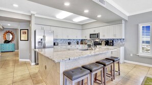 A modern kitchen with a central island, stainless steel appliances, and a tiled backsplash. - Admirals Quarters 4BR..4BA, 2120sf, STUNNING VIEWS (Orange Beach)