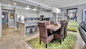 A modern kitchen with white cabinets, a dining area with wicker chairs, and a green rug. - Admirals Quarters 4BR..4BA, 2120sf, STUNNING VIEWS (Orange Beach)