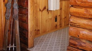 Interior de una cabaña de madera con una puerta, esquíes apoyados en la pared y una toalla colgando.