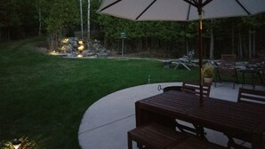 A patio with a table and chairs, an umbrella, and a stone feature with lights. - Peaceful, Cozy, Clean, Fun Mid-Century Stay! Backyard Oasis Waterfall, Fireplace (Fish Creek)