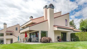A modern two-story house with a covered patio, a chimney, and a well-maintained lawn.