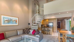 A spacious living area with a curved sofa, a glass coffee table, and a spiral staircase leading to an upper level.
