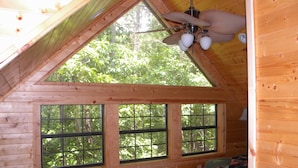 Eine Hütte mit geneigtem Dach, Deckenventilator und großen Fenstern mit Blick auf die umliegenden Bäume.