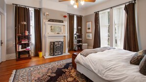 Une chambre avec un grand lit, une cheminée, une bibliothèque et une vue sur l’extérieur.
