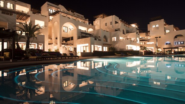 Ein Hotel bei Nacht mit einem Swimmingpool, der die Architektur des Gebäudes spiegelt.