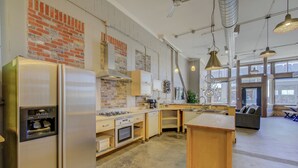 Una cocina amplia con electrodomésticos de acero inoxidable, una pared de ladrillo y ventanas grandes.