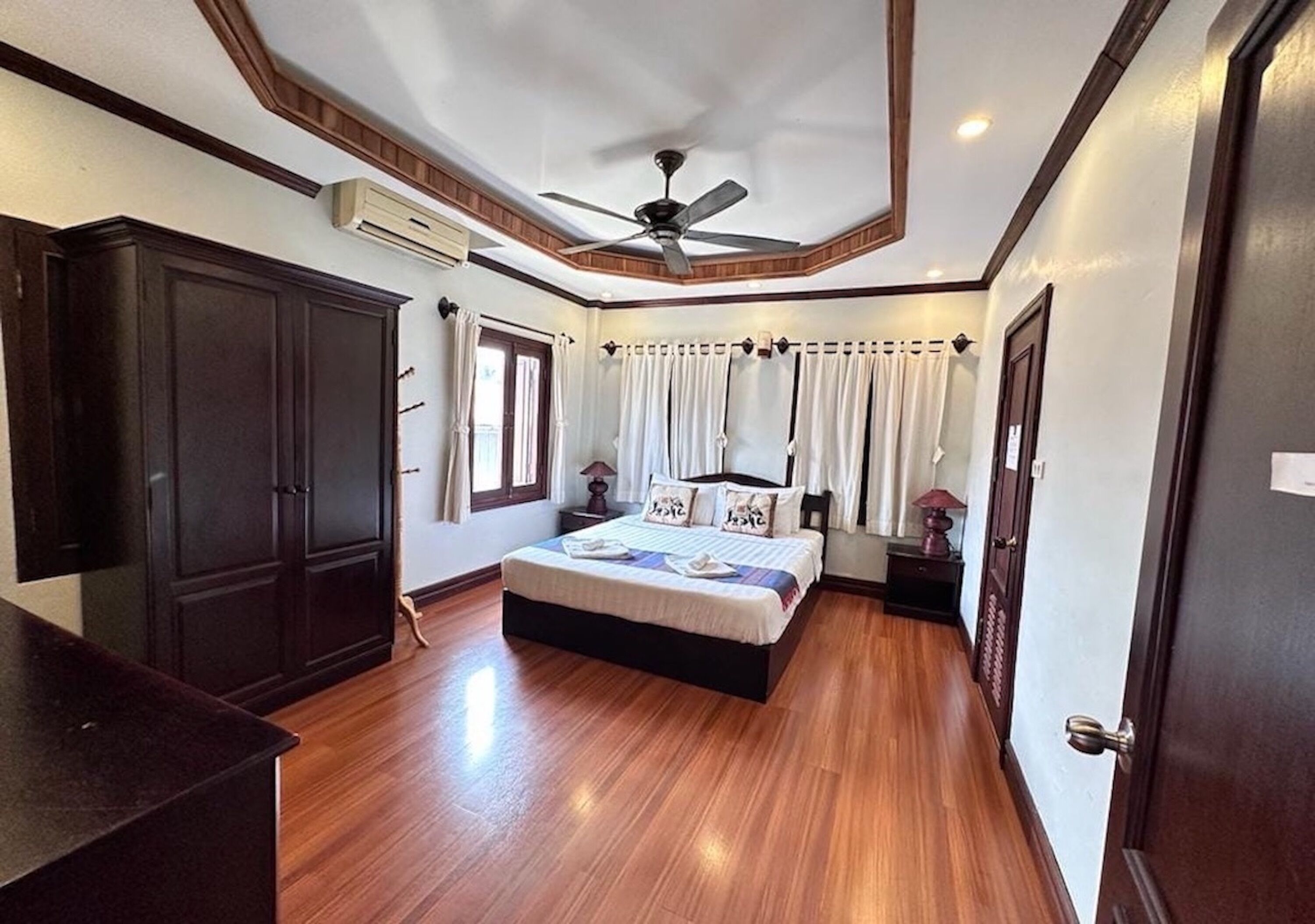 A bedroom with a bed, a ceiling fan, an air conditioning unit, and wooden flooring.