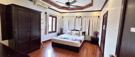 A bedroom with a bed, a ceiling fan, an air conditioning unit, and wooden flooring.