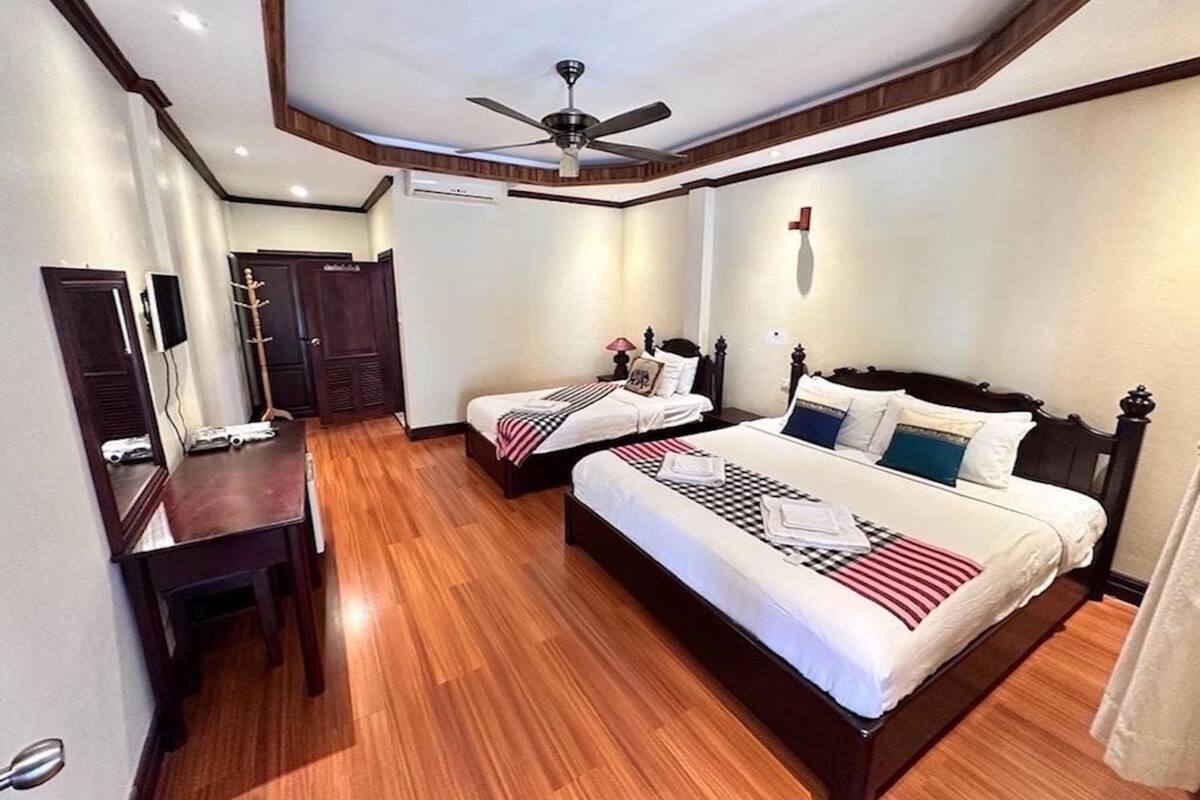 A hotel room with two beds, a desk, a ceiling fan, and a TV.