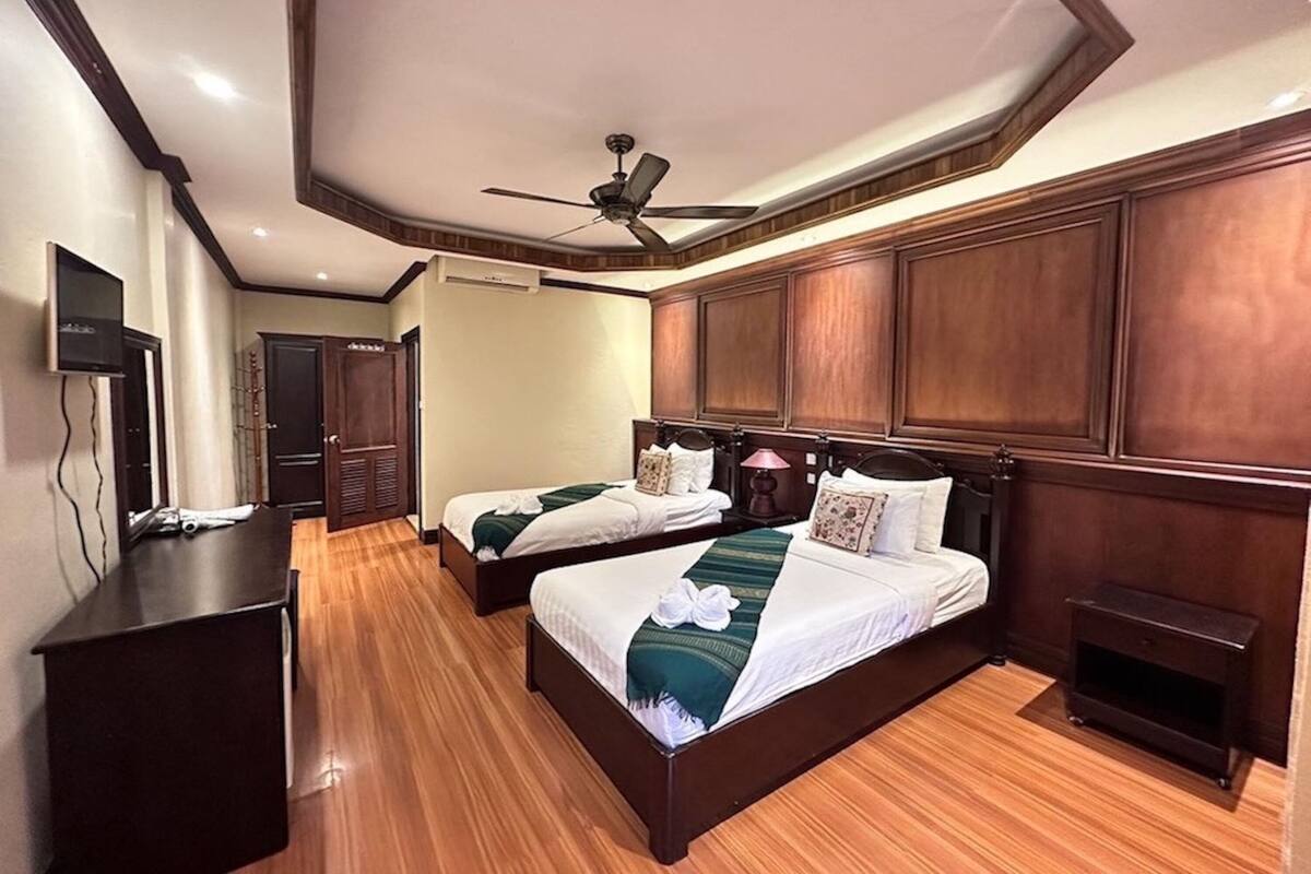 A hotel room with two beds, a desk, a ceiling fan, and wooden paneling.