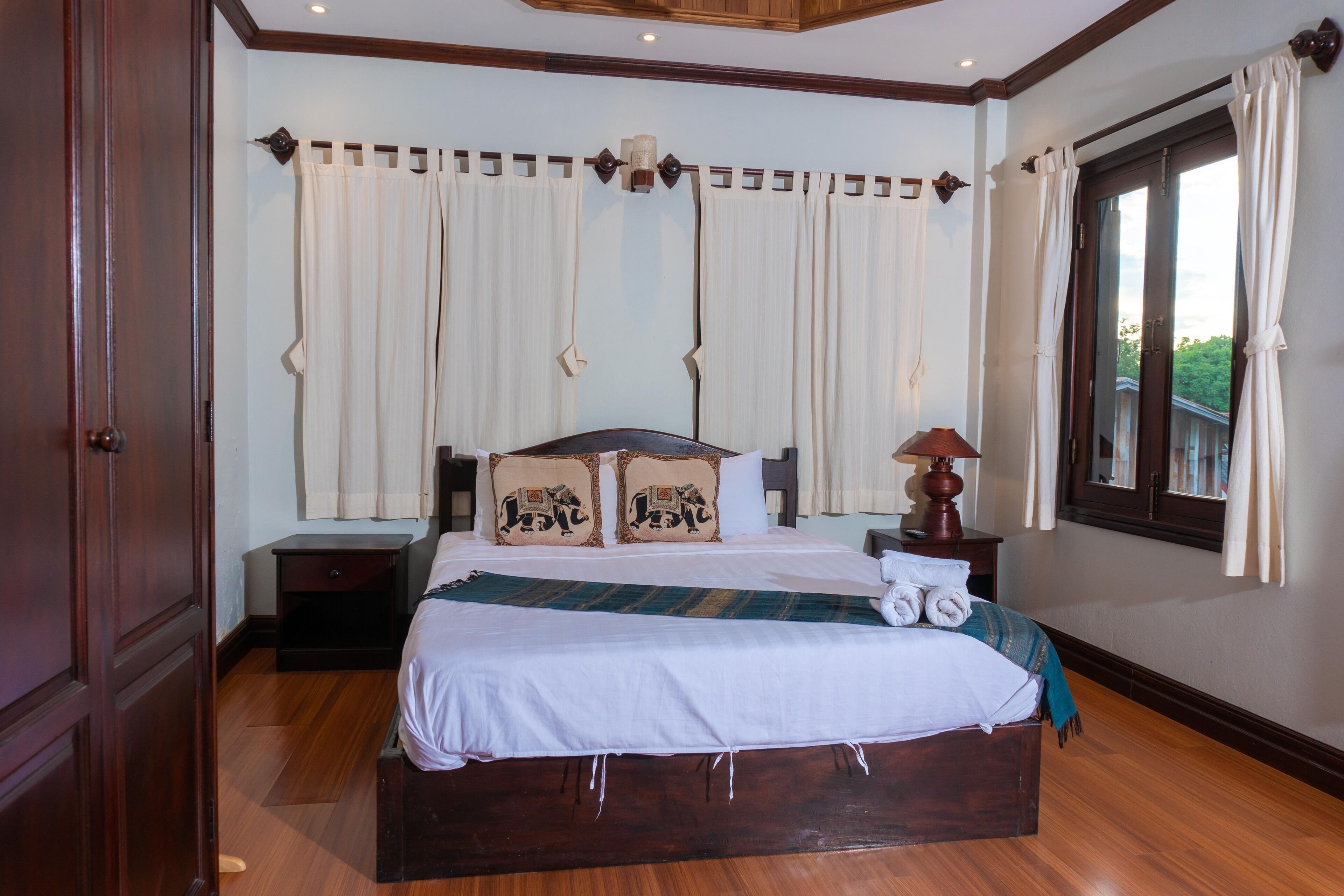 A neatly arranged bedroom with a large bed, a nightstand, a lamp, and a window with curtains.