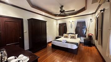 A bedroom with a bed, wooden floor, ceiling fan, wardrobe, bedside table, and a window with curtains.