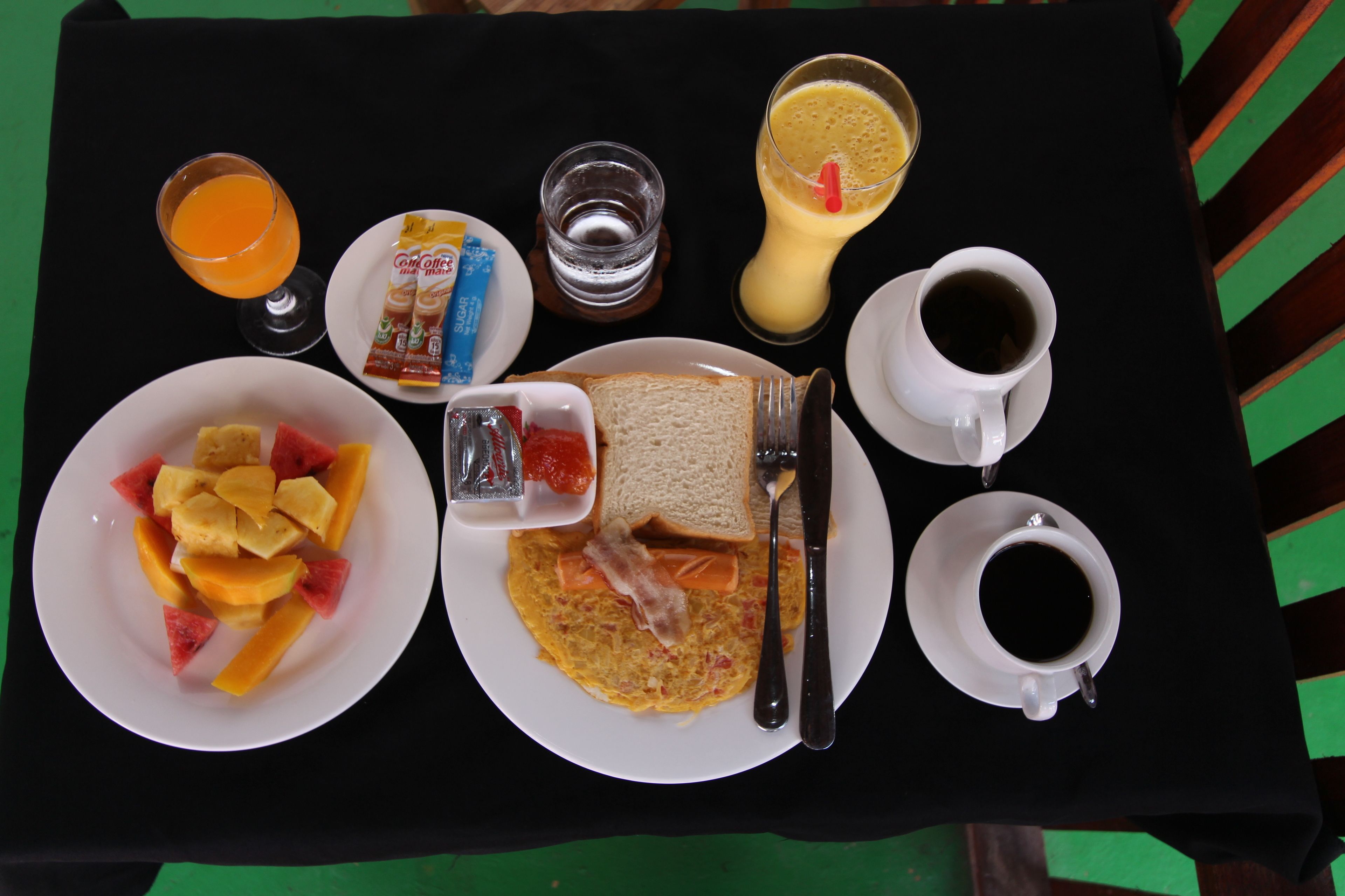 Ein Frühstückswagen mit Eiern, Toast und Obst, einem Glas Orangensaft, einem Glas Wasser, einer Tasse Kaffee und einer Zuckerportion.
