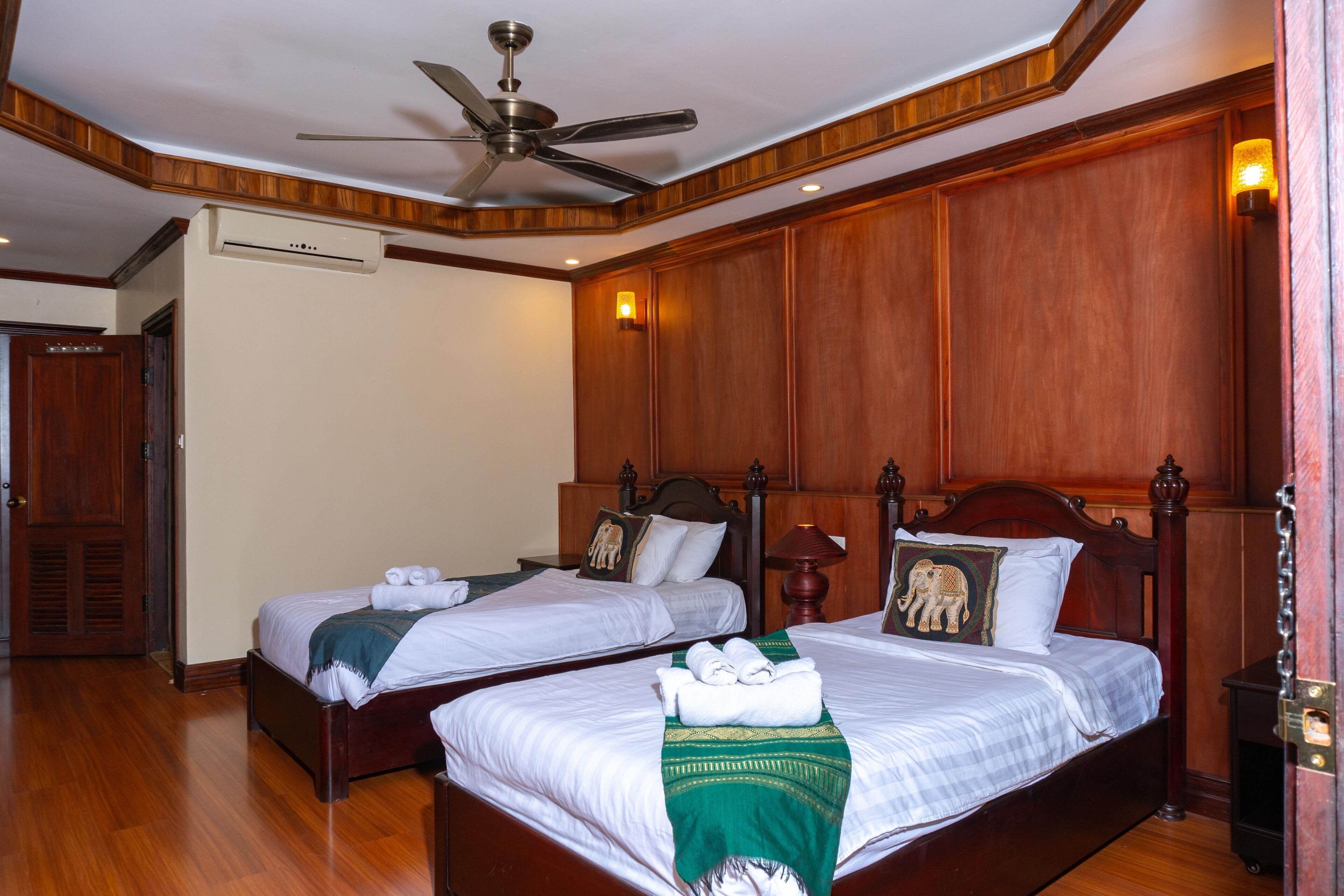 Habitación de hotel con dos camas, paneles de madera, ventilador de techo y aire acondicionado.