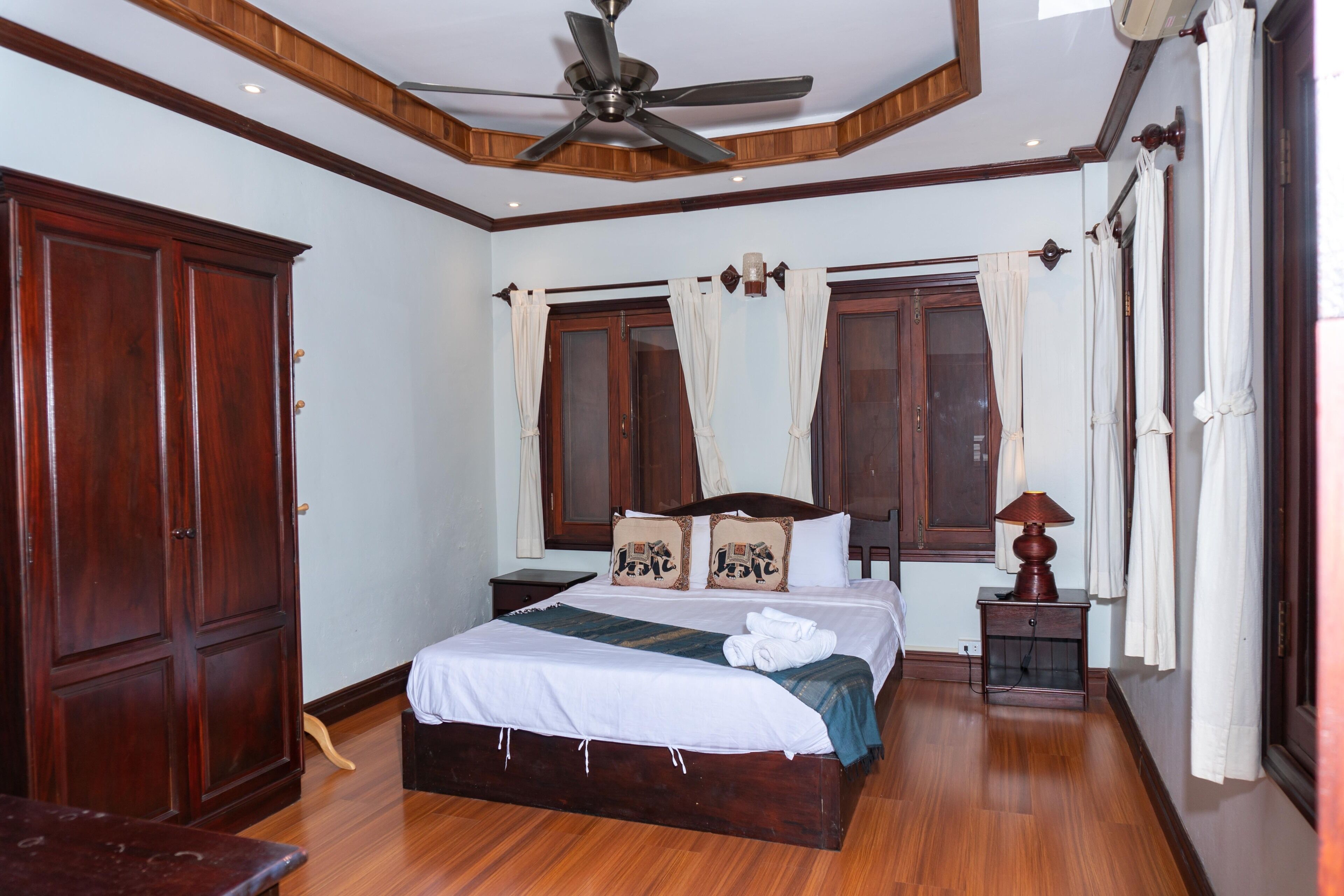 A bedroom with a wooden bed, a nightstand, a ceiling fan, and a window with curtains.