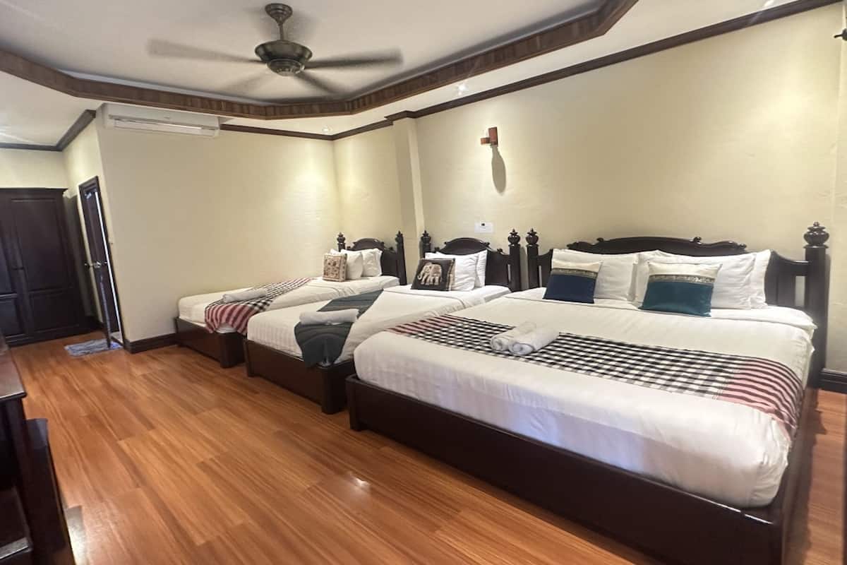 A hotel room with three beds, wooden flooring, a ceiling fan, and a door.