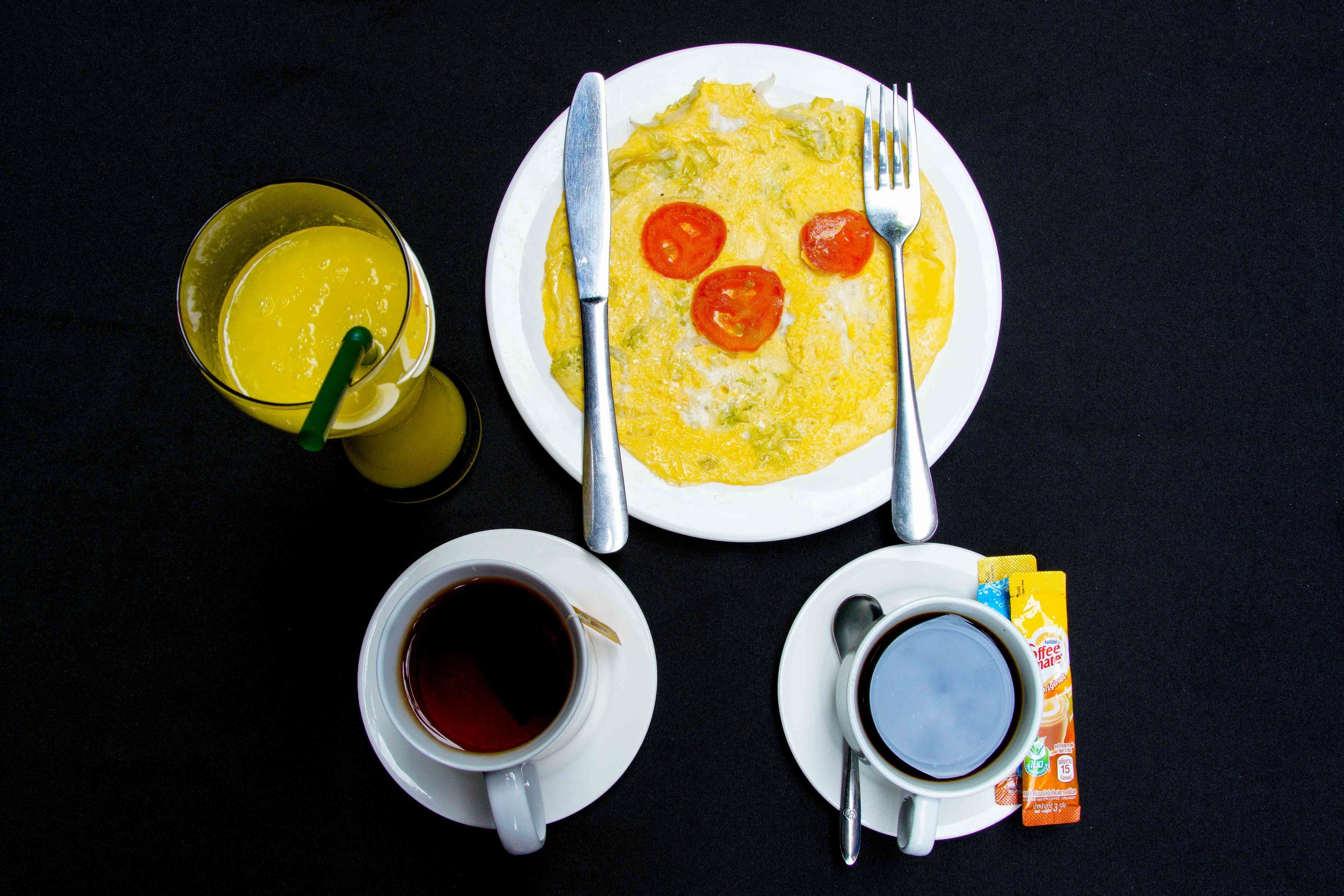A breakfast setup with an omelette, two cups of coffee, a glass of orange juice, and a packet of coffee creamer.