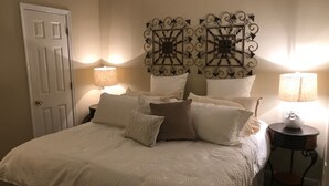 Een slaapkamer met een bed, kussens, een nachtkastje en wanddecoratie.