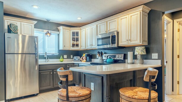 A modern kitchen with white cabinetry, a stainless steel refrigerator, a microwave, and a central island with two wicker chairs. - Piccolo Cottage -  Great Location - Walking distance to Douglas Beach! (Douglas)