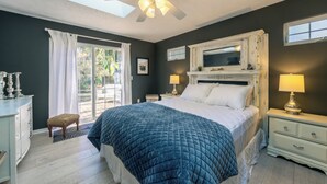 A bedroom with a large bed, a ceiling fan, a window with curtains, a nightstand with a lamp, and a dresser. - Piccolo Cottage -  Great Location - Walking distance to Douglas Beach! (Douglas)