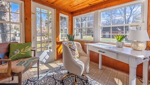 A cozy room with wooden walls and a ceiling, a white desk, a chair, a bench, and a patterned rug. - Piccolo Cottage -  Great Location - Walking distance to Douglas Beach! (Douglas)