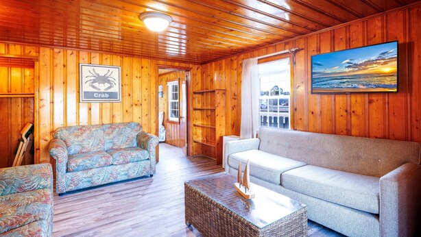 A wooden interior with two sofas, a wicker coffee table, and a framed picture of a sunset. - Beach Cottage Heart of Ocean Drive Sleeps 14 (North Myrtle Beach)