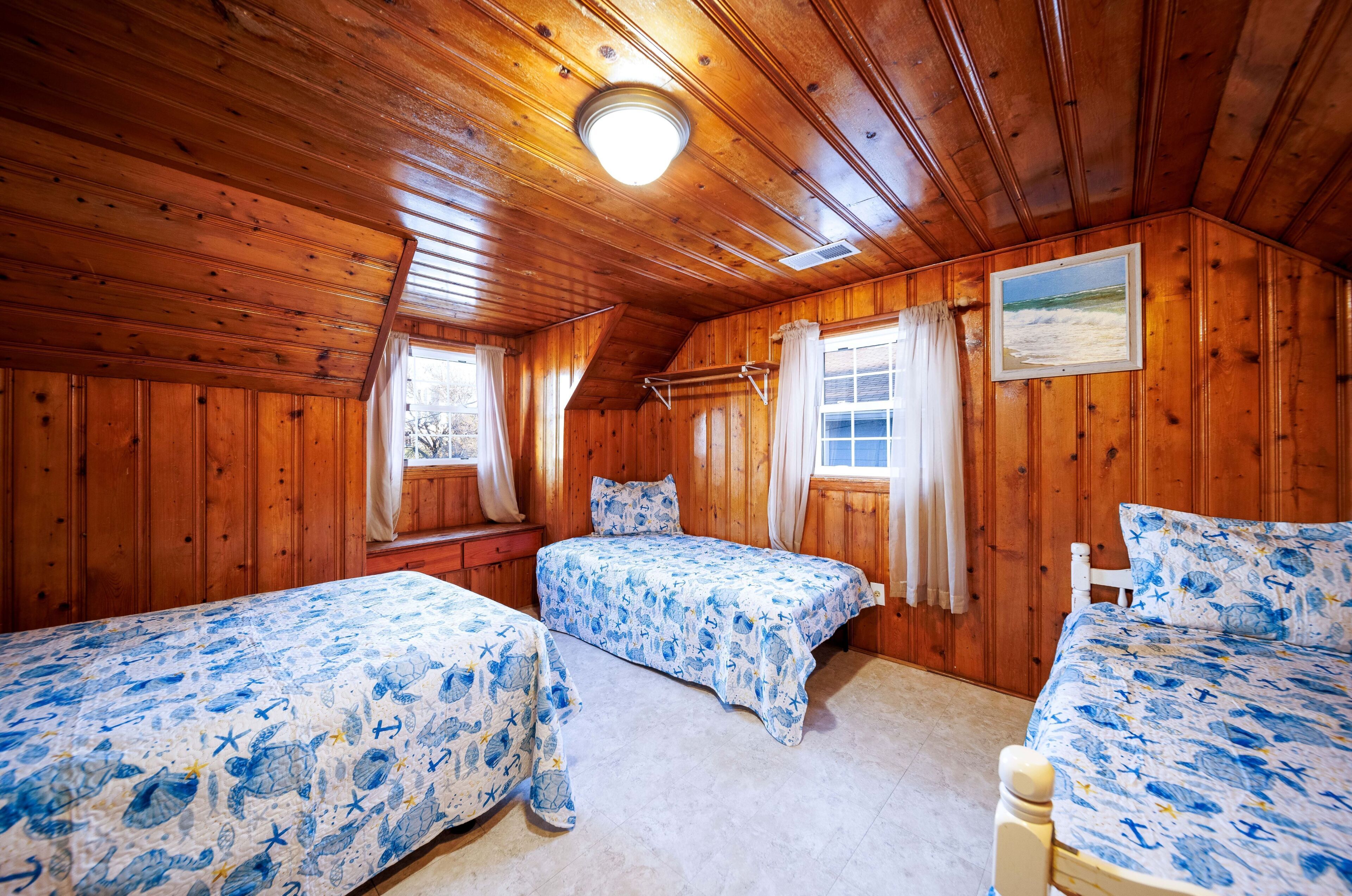 A cabin with two beds, wooden walls, a ceiling light, and a window with curtains.