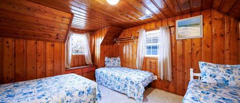A cabin with two beds, wooden walls, a ceiling light, and a window with curtains.