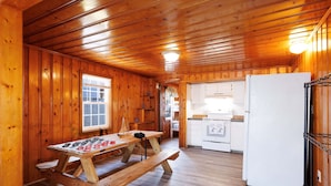 A wooden interior with a wooden table and benches, a white refrigerator, and a kitchen area with white cabinets and appliances. - Beach Cottage Heart of Ocean Drive Sleeps 14 (North Myrtle Beach)
