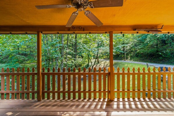 A covered outdoor area with a wooden fence, a ceiling fan, and a view of a forested area. - Honeymoon, private settings, 10 min from main street, family fun, fishing pond (Sevierville)