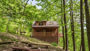 Une cabane dotée d’une terrasse en bois, entourée d’arbres et comprenant un foyer extérieur.