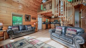 Een houten chalet interieur met twee leren banken, een eethoek en een spiltrap.