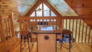 Un intérieur en bois avec un plafond en pente, deux tabourets de bar et une table équipée d’un ordinateur.