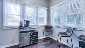 Quarto com duas janelas amplas, uma cafeteira, um armário de metal com gavetas e uma única cadeira.
