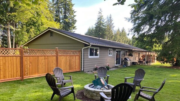 A backyard with a fire pit, four Adirondack chairs, and a wooden fence. - Cozy, 3 bedroom home- ideal for couples or families (Forks)