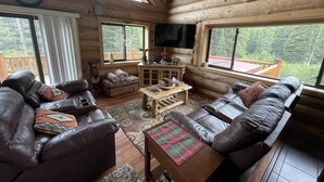 Ein rustikales Blockhaus-Interieur mit Ledersofas, einem Holztisch und einem an der Wand montierten Fernseher.