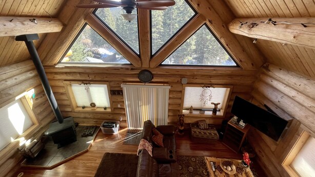 Ein gemütliches Blockhaus-Interieur mit Holzbalkendecke, Kamin, Sofa und Fernseher.